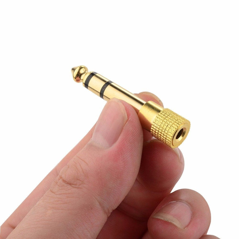 Gold 6.5mm to 3.5mm headphone jack adapter held in hand, close-up view