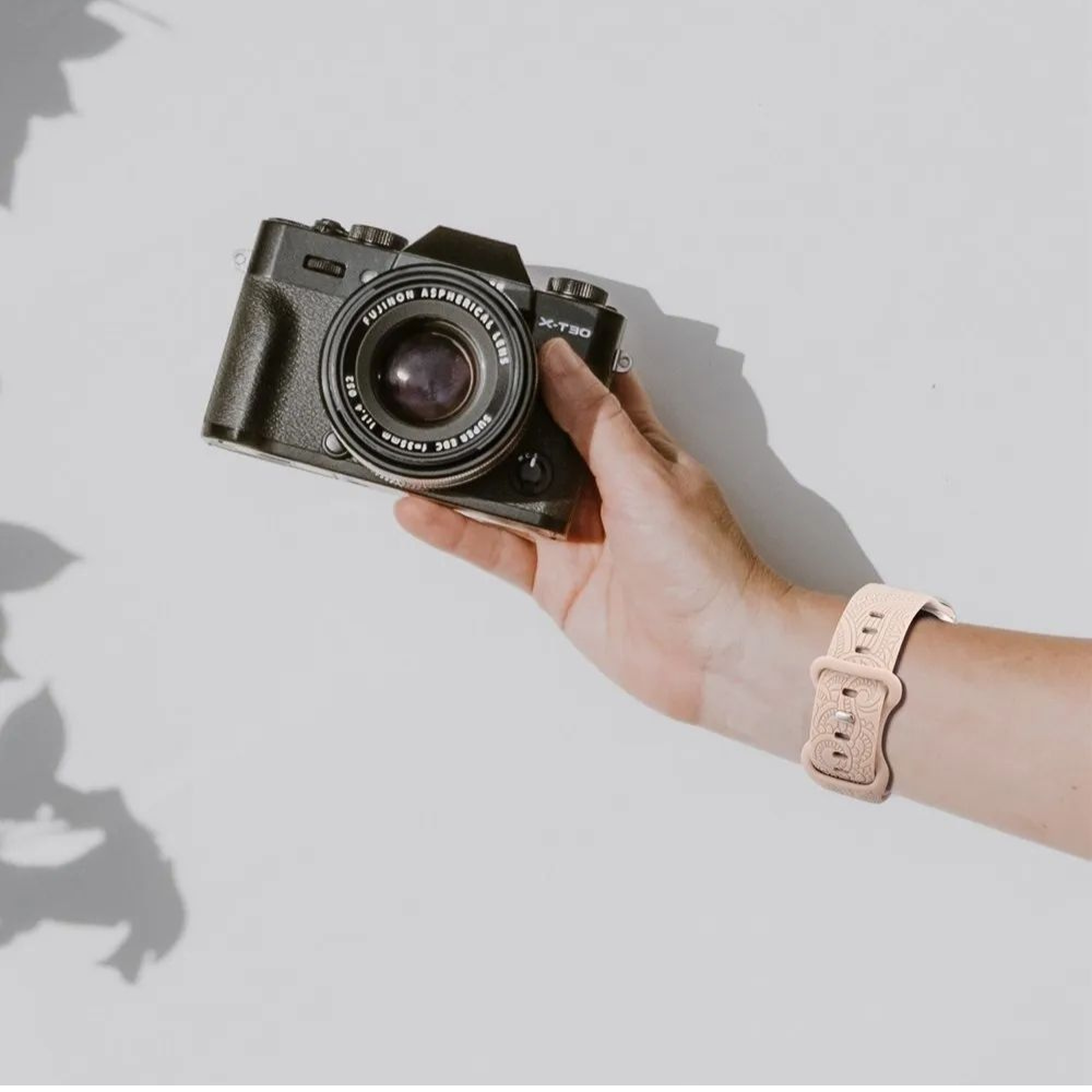 Hand holding Fujifilm X-T30 camera wearing engraved floral silicone Apple Watch band in light pink nude, bohemian style wristband