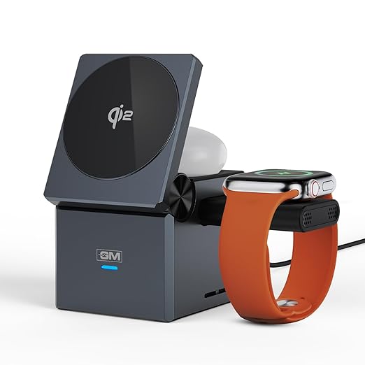 A dark gray multi-device wireless charging stand with a square charging pad, a rectangular charging base, and a side connector, shown charging a white wireless earbud and an orange smartwatch band with a black smartwatch. The brand 'GM' is visible on the front of the stand.