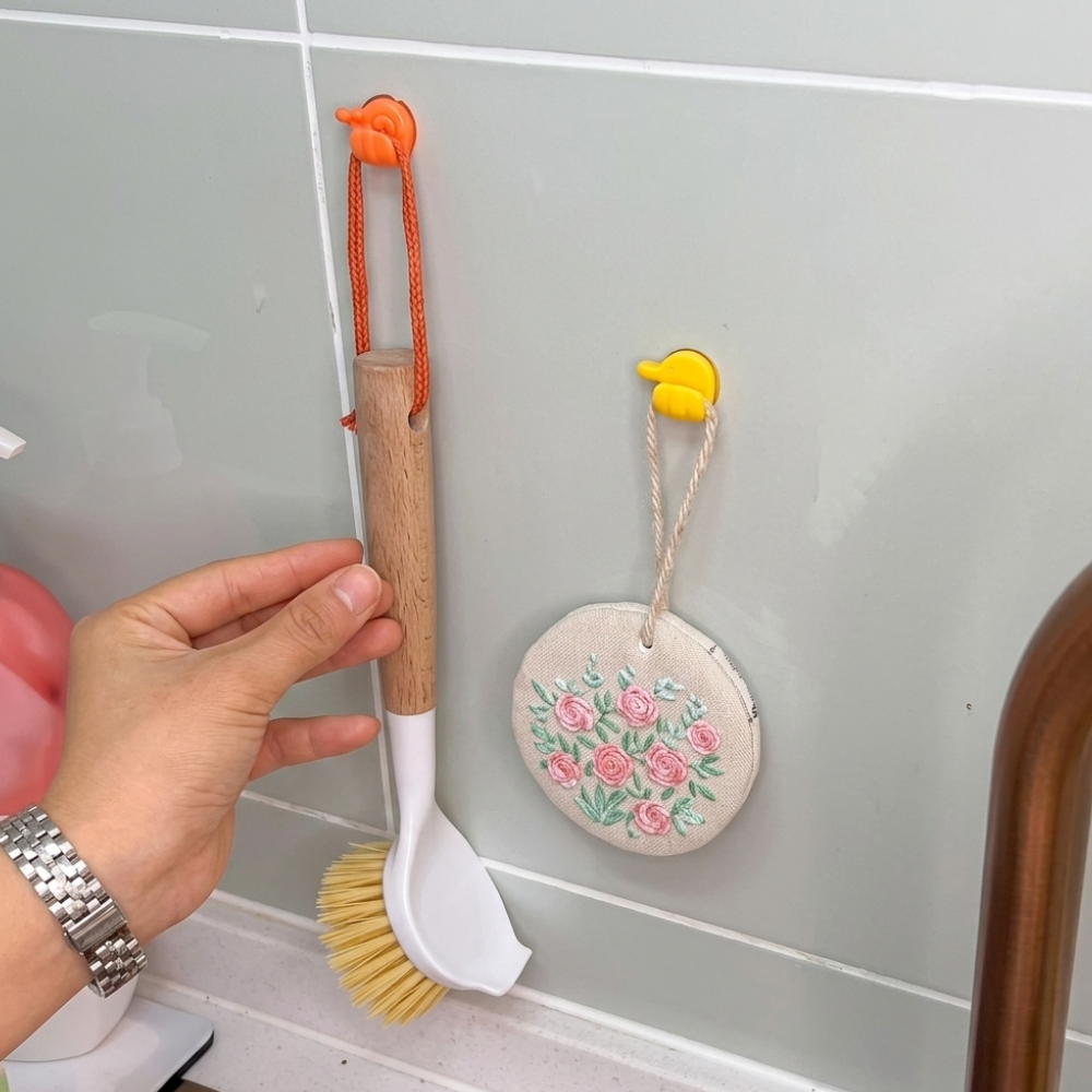 Hand holding a kitchen brush with a floral decoration on a tiled wall.