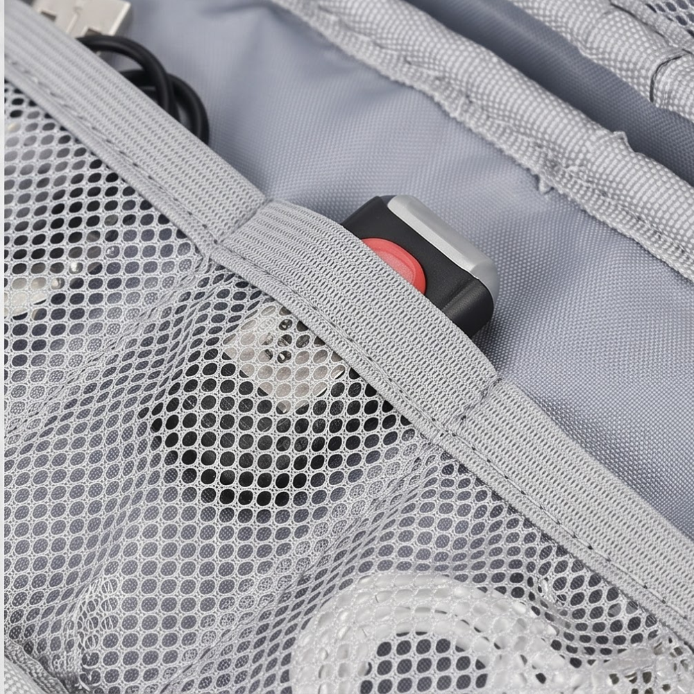 Close-up of a gray mesh pocket inside a light gray bag, with a black and red strap or buckle visible along the zipper trim.